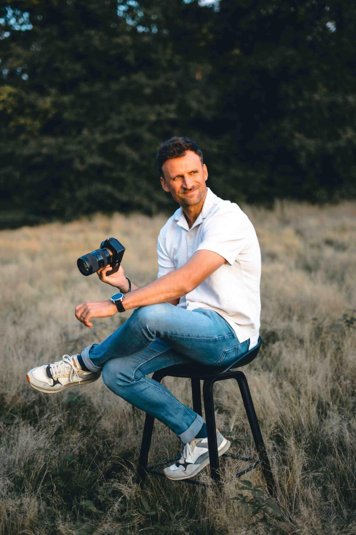 Portret van Nanou, trouwfotograaf uit Keerbergen, zittend op een kruk in het hoge gras met een camera in de hand